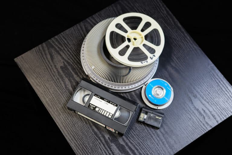 Camera reel, VHS tape, video tape, and DVD disks on table representing media conversion